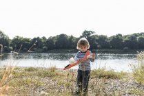 Garçon jouer avec jouet avion au bord de la rivière — Photo de stock
