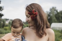 Mother with flower in her hair holding baby in garden — Stock Photo