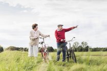 Pareja mayor con bicicletas paseando por el paisaje rural - foto de stock