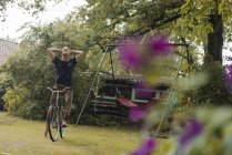Hombre maduro con bicicleta disfrutando de la lluvia de verano en el jardín - foto de stock