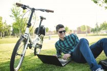 Young man with bicycle using laptop in a park — Stock Photo