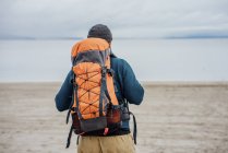 Вид сзади на человека с большим оранжевым рюкзаком у озера — стоковое фото