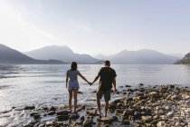 Молода пара йде рука об руку на березі озера — стокове фото