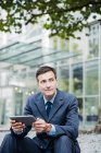 Businessman using tablet in city and looking away — Stock Photo