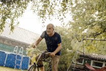 Счастливый взрослый мужчина катается на велосипеде в летний дождь в саду — стоковое фото