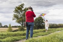 Senior man filming wife flying kite in rural landscape — Stock Photo