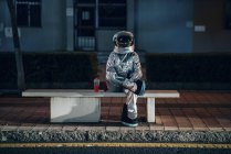 Homem do espaço sentado no banco na paragem de autocarro à noite com refrigerante — Fotografia de Stock