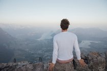Switzerland, Grosser Mythen, young man on a hiking trip sitting on a rock at sunrise — Stock Photo