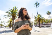 Улыбающаяся девочка-подросток держит смартфон на набережной — стоковое фото