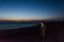 Jeune femme utilisant un smartphone sur la plage au crépuscule — Photo de stock