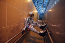 Spaceman in city at night with takeaway coffee sitting on railing in narrow passageway — Stock Photo