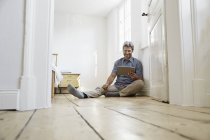 Homme mûr assis sur le sol de la chambre à coucher, en utilisant une tablette numérique — Photo de stock