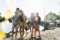 Gruppo di amici felici con i telefoni cellulari che camminano lungo il fiume — Foto stock