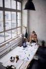 Woman standing at desk in a loft and looking through window — Stock Photo