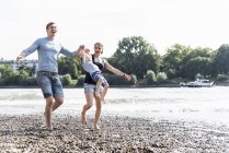 Heureuse famille marchant au bord de la rivière le jour d'été — Photo de stock