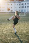 Молода жінка грає в футбол на футбольному грунті балансування м'яч — стокове фото