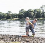 Père et fils s'amusent au bord de la rivière, jouant avec un pistolet à eau — Photo de stock