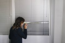 Жінка, що стоїть за вікном, шпигунство через жалюзі — стокове фото