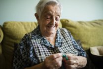 Портрет улыбающейся пожилой женщины, вяжущейся на диване дома — стоковое фото