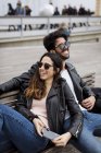 España, Barcelona, feliz pareja joven con teléfono celular descansando en un banco de la ciudad - foto de stock