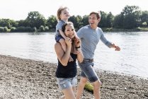 Família feliz andando na beira do rio no dia ensolarado de verão — Fotografia de Stock