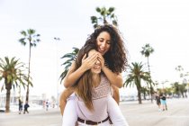 Two happy playful female friends on promenade with palms — Stock Photo