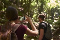 Женщина фотографирует с телефоном своего парня в лесу — стоковое фото