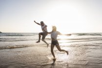 Jeune couple s'amusant sur la plage du coucher du soleil, éclaboussant l'eau dans la mer — Photo de stock