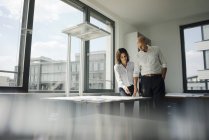 Dos arquitectos trabajando en la oficina, discutiendo planos en la ventana - foto de stock