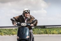 Hombre mayor activo exceso de velocidad en scooter en carretera de campo - foto de stock