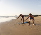 Молодой человек показывает молодой женщине, как заниматься серфингом на песчаном пляже — стоковое фото