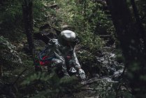 Spaceman exploring nature, crouching at brook in forest — Stock Photo