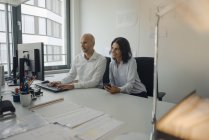 Businessman and woman working together in office at desk with computer — Stock Photo