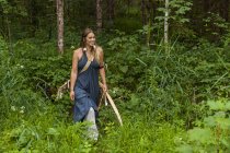 Mulher sorridente andando em uma floresta com arco e flecha — Fotografia de Stock