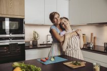 Glückliches lesbisches Paar steht in Küche mit Schürzen — Stockfoto