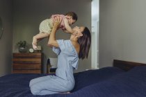 Madre levantando a su bebé en la cama - foto de stock