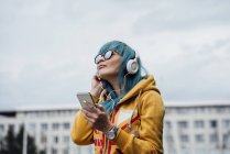 Ritratto di giovane donna con capelli tinti di blu che ascolta musica con smartphone e cuffie — Foto stock