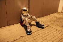 Spaceman sitting at metal wall at night — Stock Photo