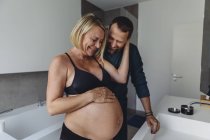 Счастливая беременная пара смотрит на живот в ванной комнате — стоковое фото