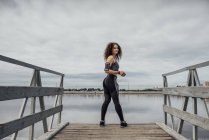 Giovane donna atletica in piedi sul molo a riva del fiume — Foto stock