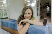 Улыбающаяся взрослая женщина на диване дома смотрит в сторону — стоковое фото