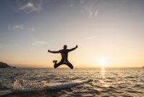 Молодий чоловік, який стрибає з приладдя у воду на заході сонця — стокове фото