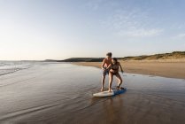 Hombre joven mostrando a mujer joven cómo surfear en la playa - foto de stock