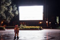 Spaceman in piedi sulla piazza di notte attratto da brillante schermo di proiezione — Foto stock