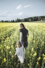 Зворотній вигляд маленької дівчинки ходьба з матір'ю в області ріпаку — стокове фото