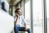 Heureux jeune homme occasionnel écoutant de la musique avec écouteurs à la fenêtre — Photo de stock