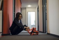 Femme d'affaires mature assise dans un couloir de bureau, mettant des patins à roulettes sur les pieds — Photo de stock
