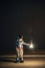 Spaceman standing on road at night and holding sparkler — Stock Photo