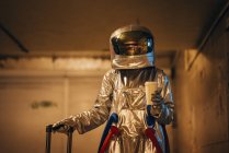 Космонавт в городе ночью стоит в подземке с чемоданом и кофе на вынос — стоковое фото