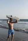 Молодой человек, идущий по пляжу с доской для серфинга — стоковое фото